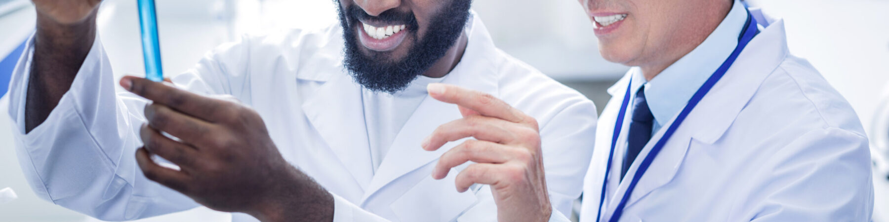 Professional scientists. Pleasant nice positive scientist standing behind his colleague and smiling while looking at the test tube